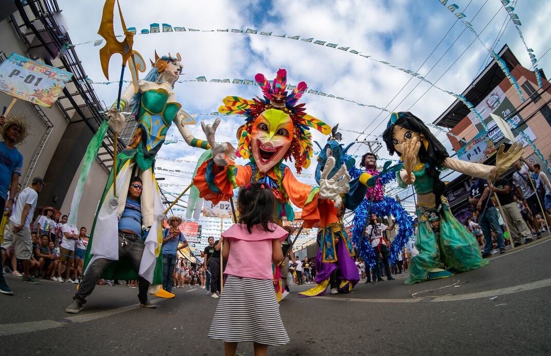A child is dwarfed by stilt-wearing performers at a Carnival parade