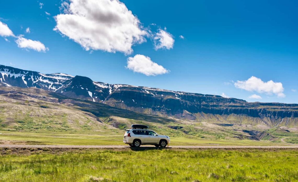 A 4x4 car parked on the side of the road in beautiful, sunny Iceland with mountains in the background