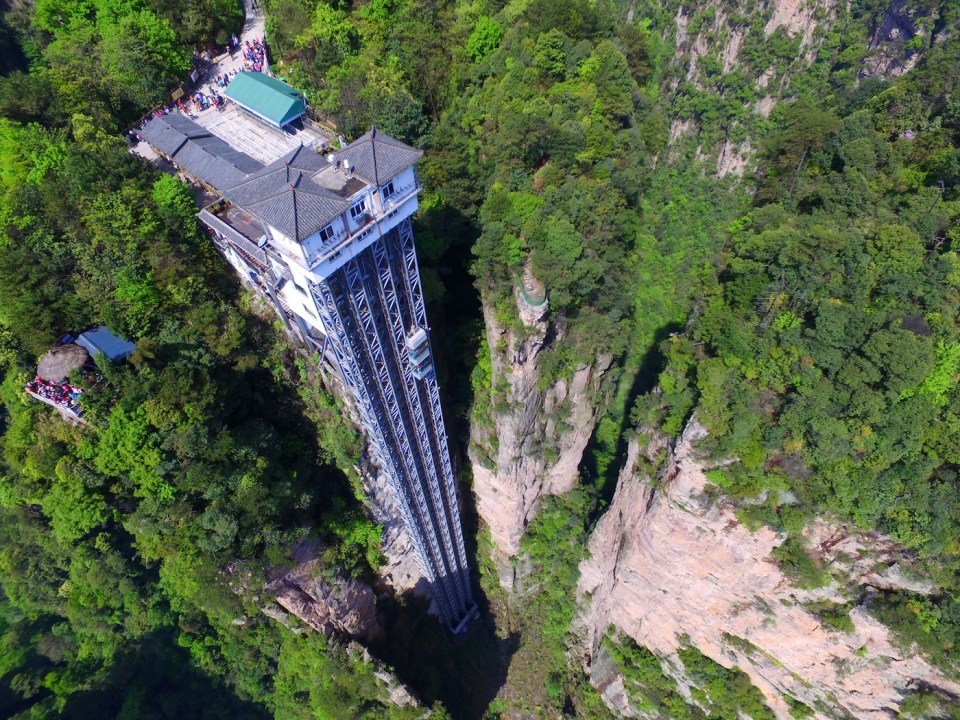 Aerial view of the Bailong Elevator, also known as the Hundred Dragons Elevator, in the Wulingyuan area of Zhangijiajie scenic spot in central China's Hunan province, 21 April 2016. China's Bailong Elevator takes visitors up 1,070ft in around a minute. The Bailong Elevator, also known as the Hundred Dragons Elevator, carries tourists 1,070ft (330m) up the side of a massive sandstone column in a mountain range in China's Hunan province. Riding the glass lift, which carries up to 50 people at a time or 1,380 an hour, offers jaw-dropping, not to say vertiginous, views down to the bottom of the rocky mountain range in the Wulingyuan area of Zhangijiajie. Work began on the lift, which cost 120m yuan in 1999 and finished in 2002. Bailong Elevator has set three Guinness world Records i.e. World's tallest full-exposure outdoor elevator, world's tallest double-deck sightseeing elevator and world's fastest passenger traffic elevator with biggest carrying capacity but due to the potential harm caused to the surrounding landscape, its future remains uncertain.
