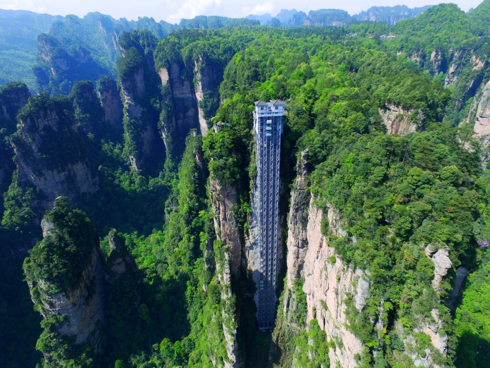 Aerial view of the Bailong Elevator, also known as the Hundred Dragons Elevator, in the Wulingyuan area of Zhangijiajie scenic spot in central China's Hunan province, 21 April 2016. China's Bailong Elevator takes visitors up 1,070ft in around a minute. The Bailong Elevator, also known as the Hundred Dragons Elevator, carries tourists 1,070ft (330m) up the side of a massive sandstone column in a mountain range in China's Hunan province. Riding the glass lift, which carries up to 50 people at a time or 1,380 an hour, offers jaw-dropping, not to say vertiginous, views down to the bottom of the rocky mountain range in the Wulingyuan area of Zhangijiajie. Work began on the lift, which cost 120m yuan in 1999 and finished in 2002. Bailong Elevator has set three Guinness world Records i.e. World's tallest full-exposure outdoor elevator, world's tallest double-deck sightseeing elevator and world's fastest passenger traffic elevator with biggest carrying capacity but due to the potential harm caused to the surrounding landscape, its future remains uncertain.