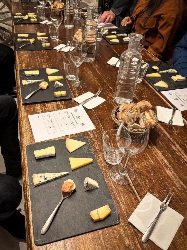 Wine and cheese tasting event at Paroles de Fromagers, showcasing a variety of French cheeses on a rustic table with wine glasses and tasting cards.
