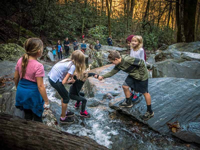 kids helping each other cross rocks over creek