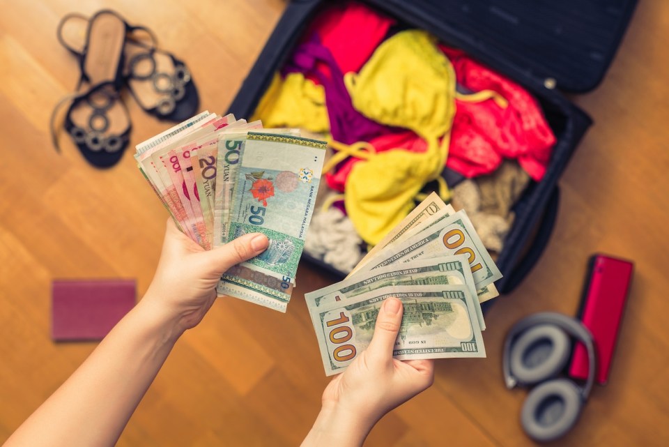 Female hands with Asian money and American hundred dollar bills. Suitcase with things on the floor