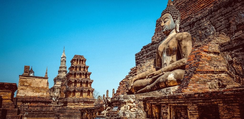 Thailand ancient temples with bright blue skies, buddha statue in foreground