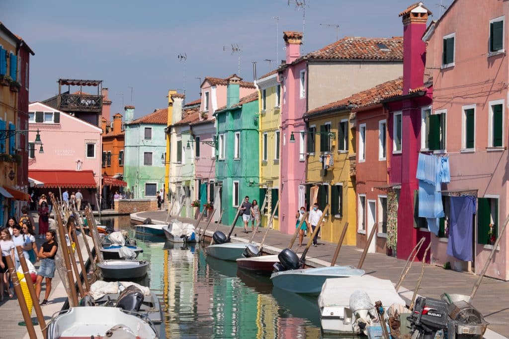Colorful streets of Burano island surrounding a canal lined with covered speedboats.