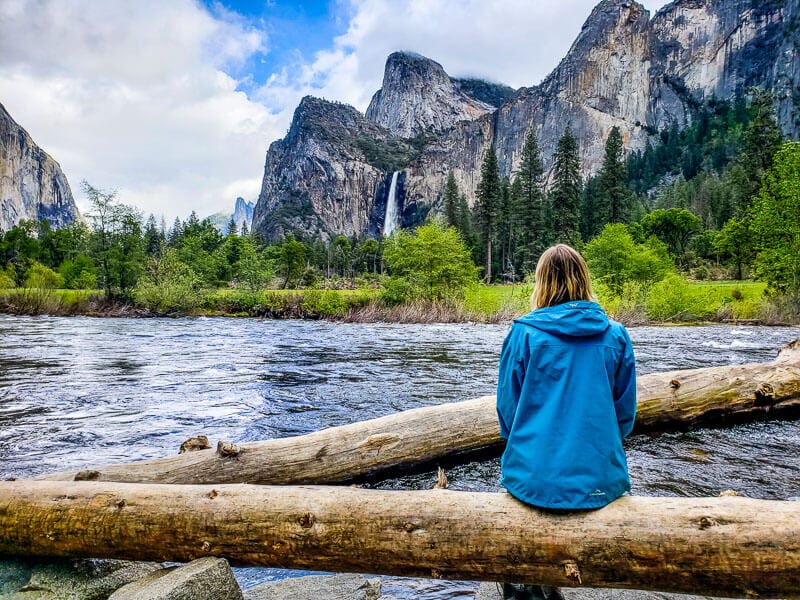 woman sitting on log looking at view of Bridalveil falls from yosemite valley