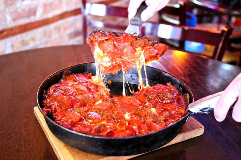 holding up a slice of deep dish pizza above the pie