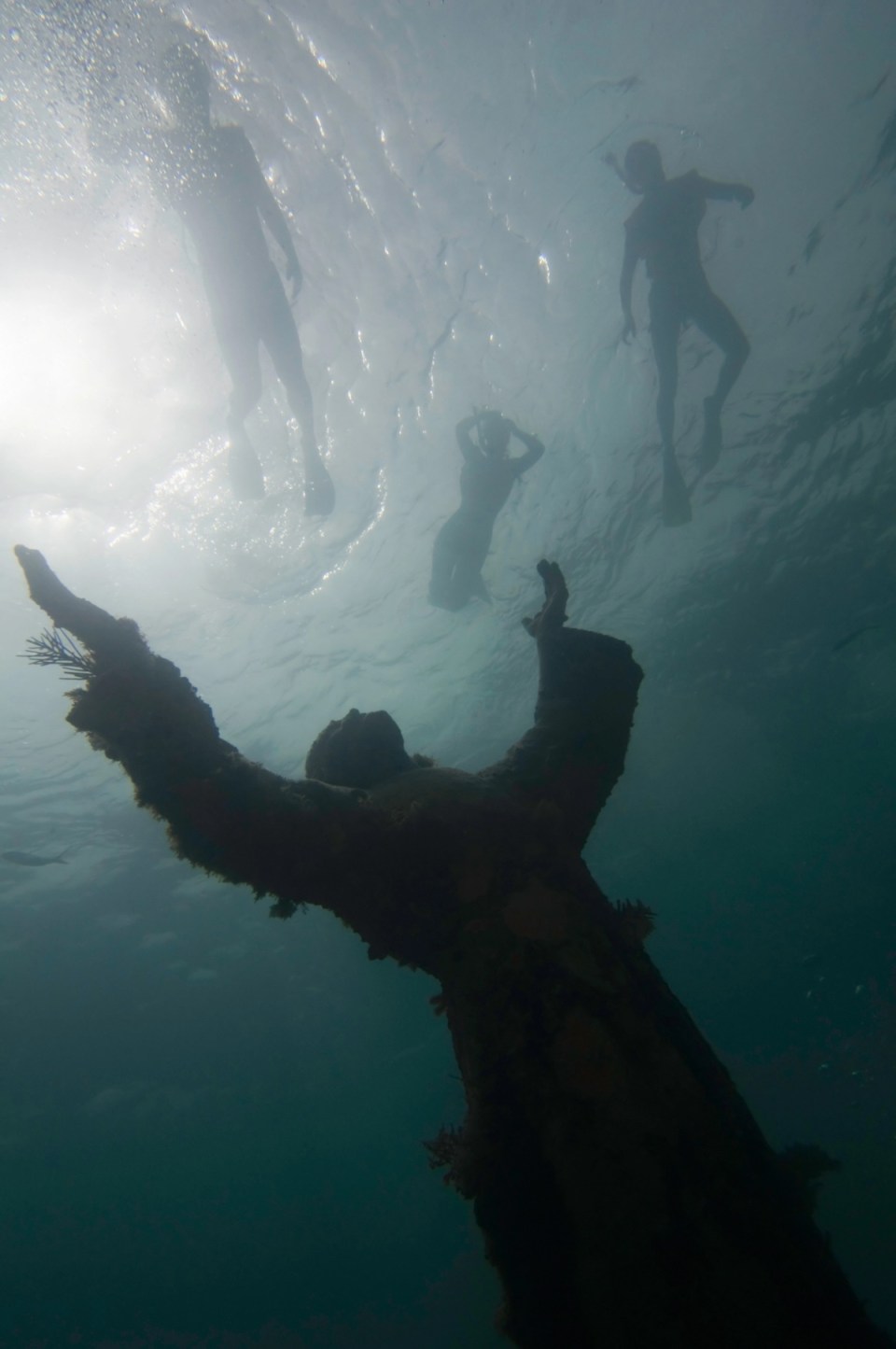 Group of snorkellers swimming over the Christ of the abyss, underwater bronze statue of Key Largo in Florida. Wide angle underwater shot against the sun, small aperture, ProPhoto RGB. Original was created by late Italian sculptor Guido Galletti and placed near Genoa, Italy. In 1965 replica was made, donated and placed in 25 feet deep waters of Key Largo in Florida. Since then it is one of the most famous and popular dive sites in USA.
