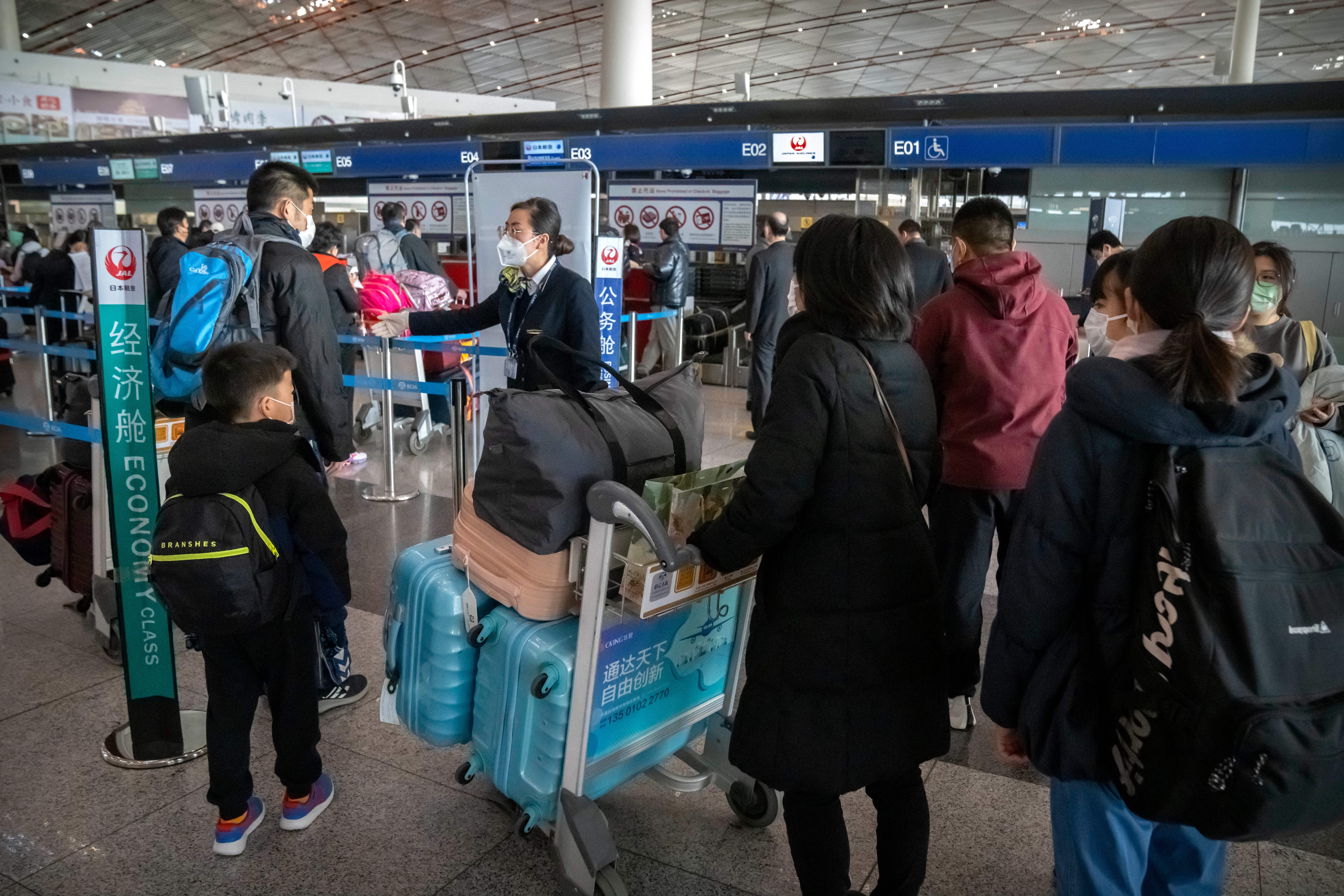 A worker directs travelers at the check-in line for a Japan Airlines flight to Tokyo at Beijing Capital International Airport