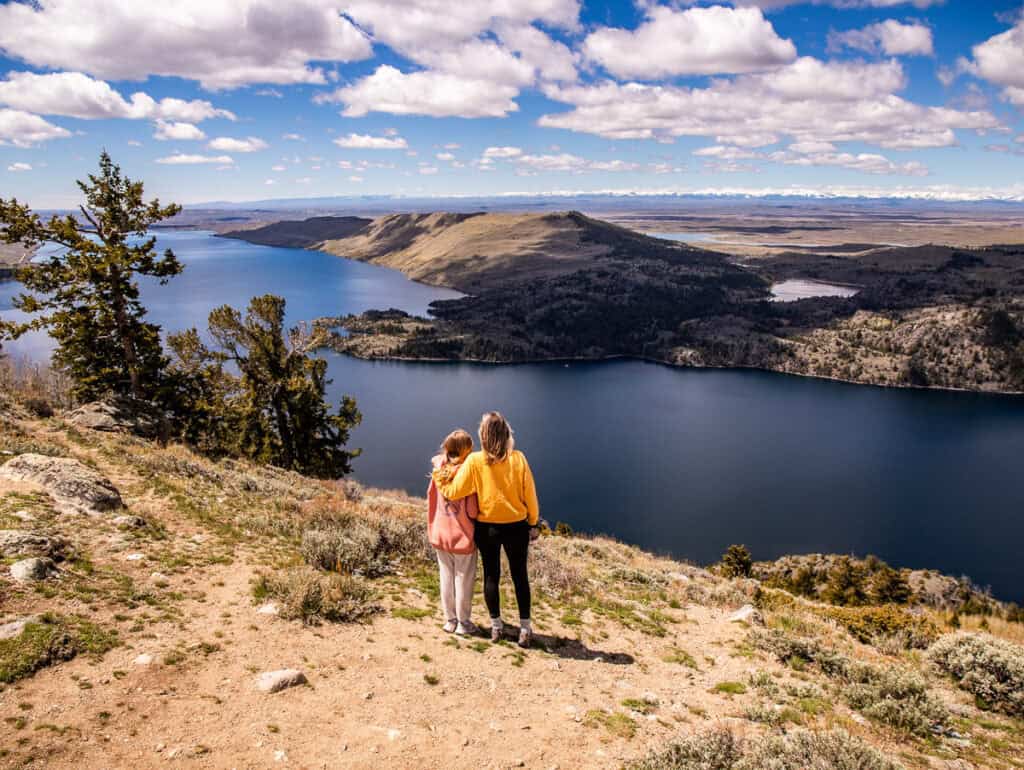 Mom and daughter standing on a mountain overlooking a lake.