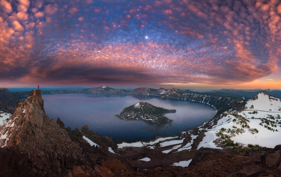 Man on hilltop viewing Crater Lake with full moon at dusk