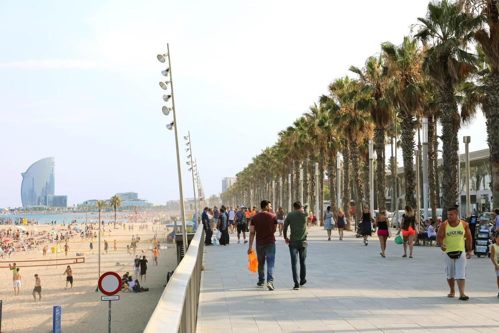 Promenade of Barceloneta beach with people enjoying sunny day in Barcelona and W hotel on background, Catalonia, Spain