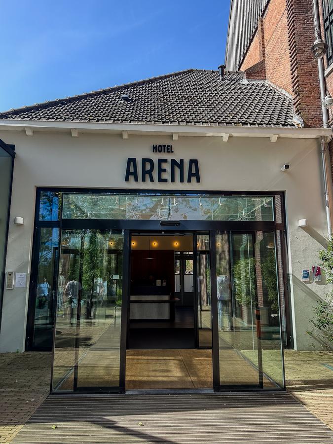 Sunny entrance of Hotel Arena with modern glass doors and elegant signage, Amsterdam.