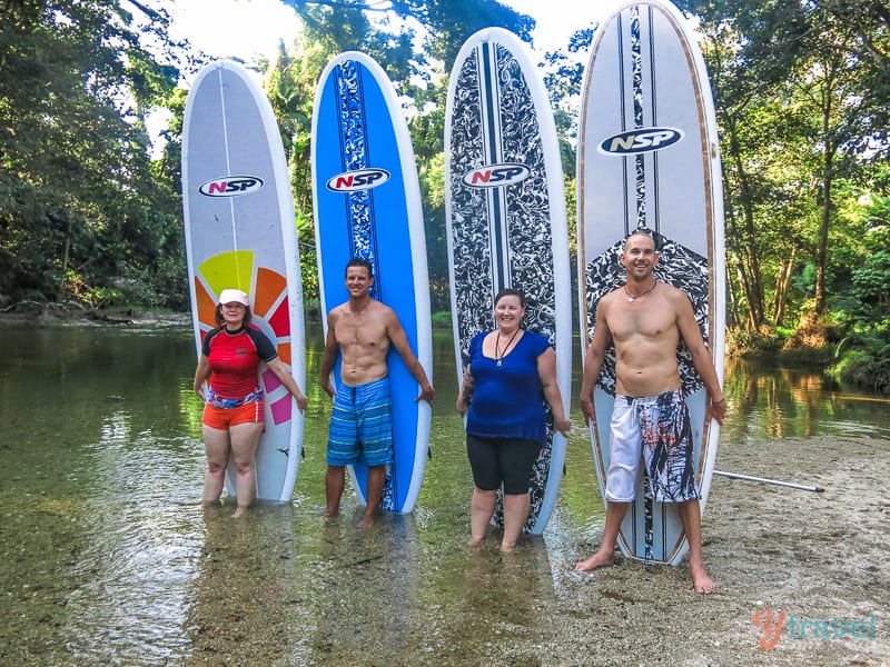 group of people standing in front of stand up paddle boards in a river