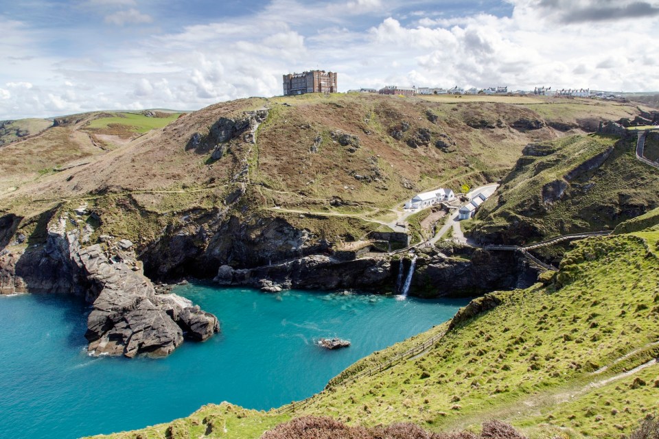 A view of the main entrance to Tintagel Castle in the valley and Hotel Camelot on the cliff. There is a beach cafe, visitors centre at the entrance.