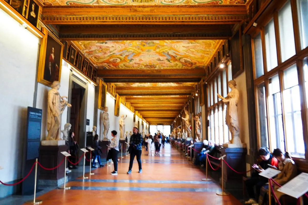 Uffizi Gallery corridor with Renaissance art and visitors in Florence