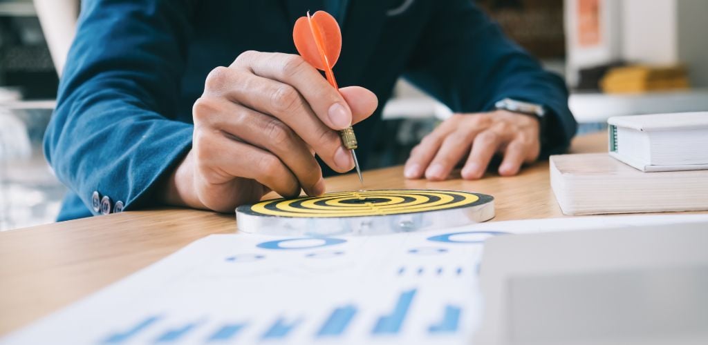 target audience, man holding a dart in the bullseye of a target, bar chart printed on paper on desk