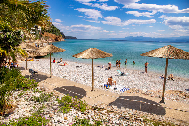 people and beach umbrellas on pebbly Arvanitia beach