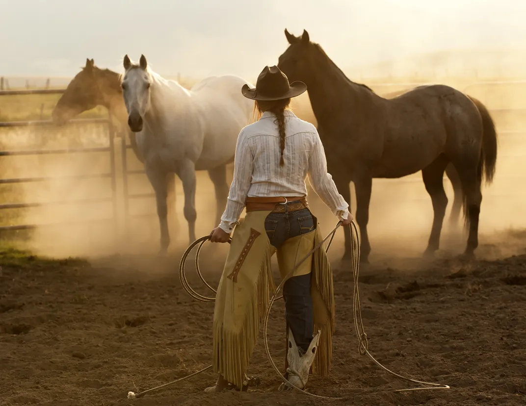 A white horse seemingly wonders what an approaching cowgirl intends to do with that lasso