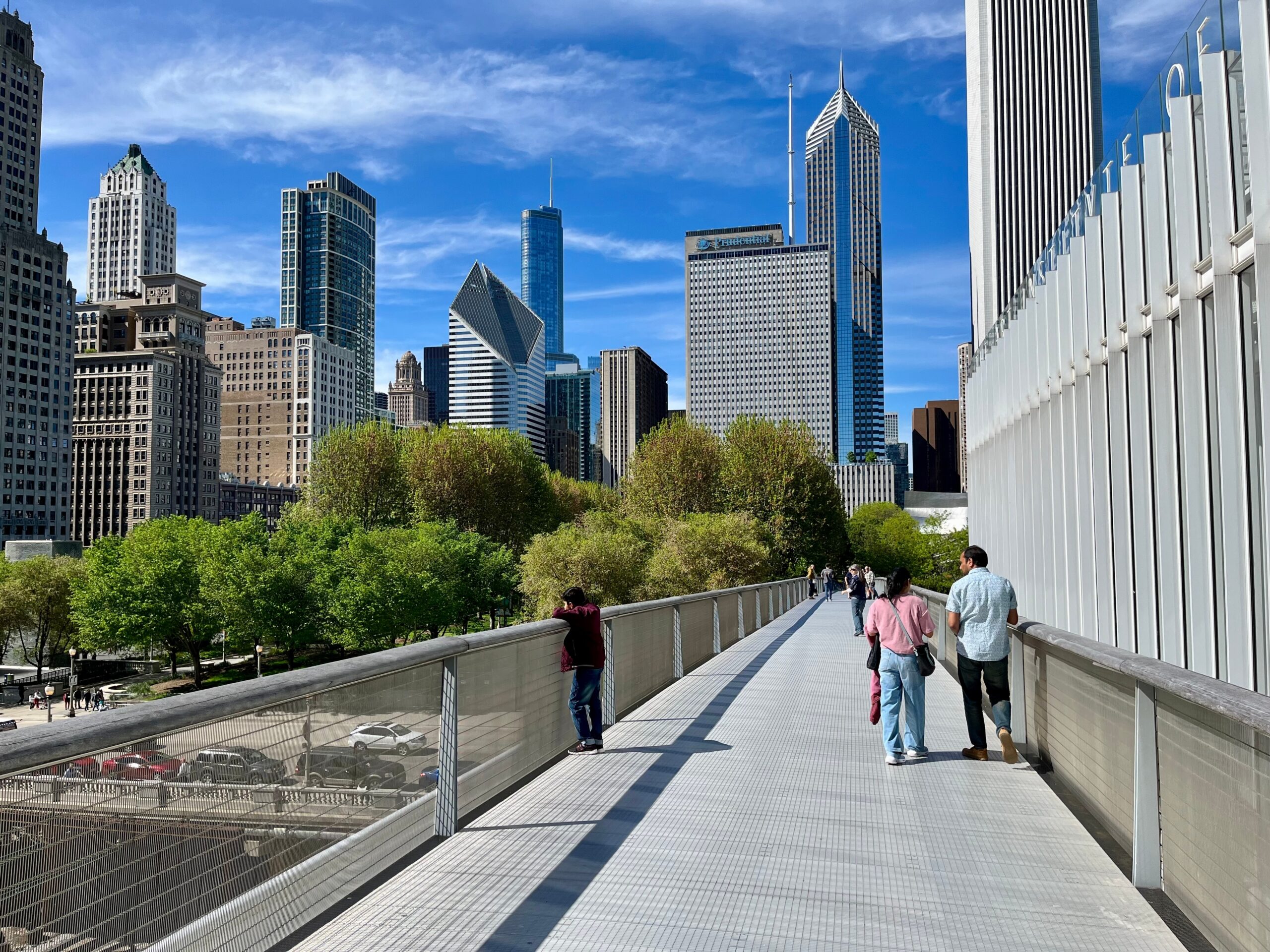 Several people walk along the elevated Nichols Bridgeway pedestrian bridge, which connects the Art Institute of Chicago with Millennium Park.