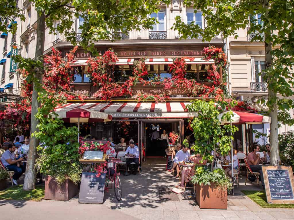 People sitting outside a pretty cafe surrounded by plants in Paris