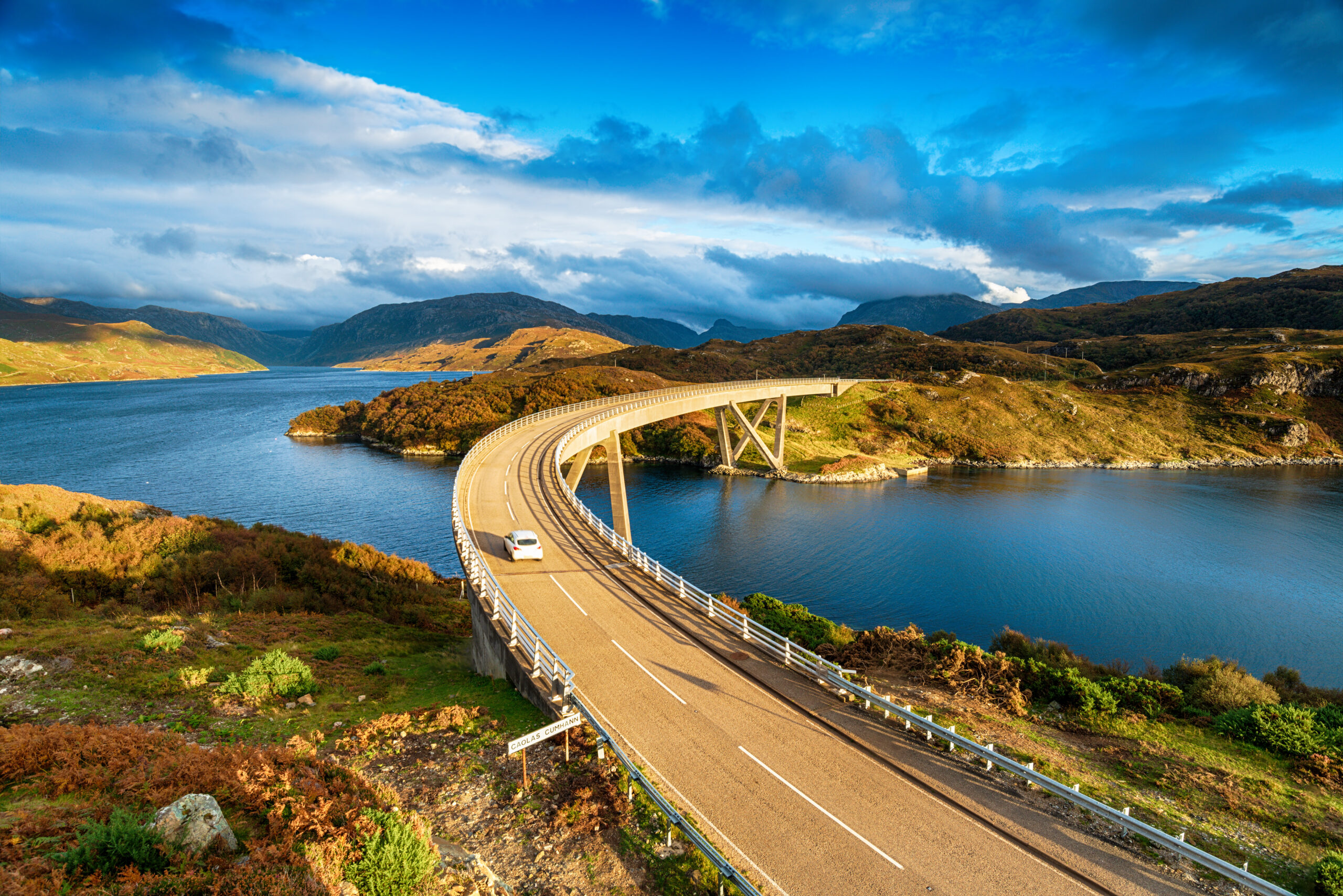 A car drives along an epic road through the Scottish Highlands.