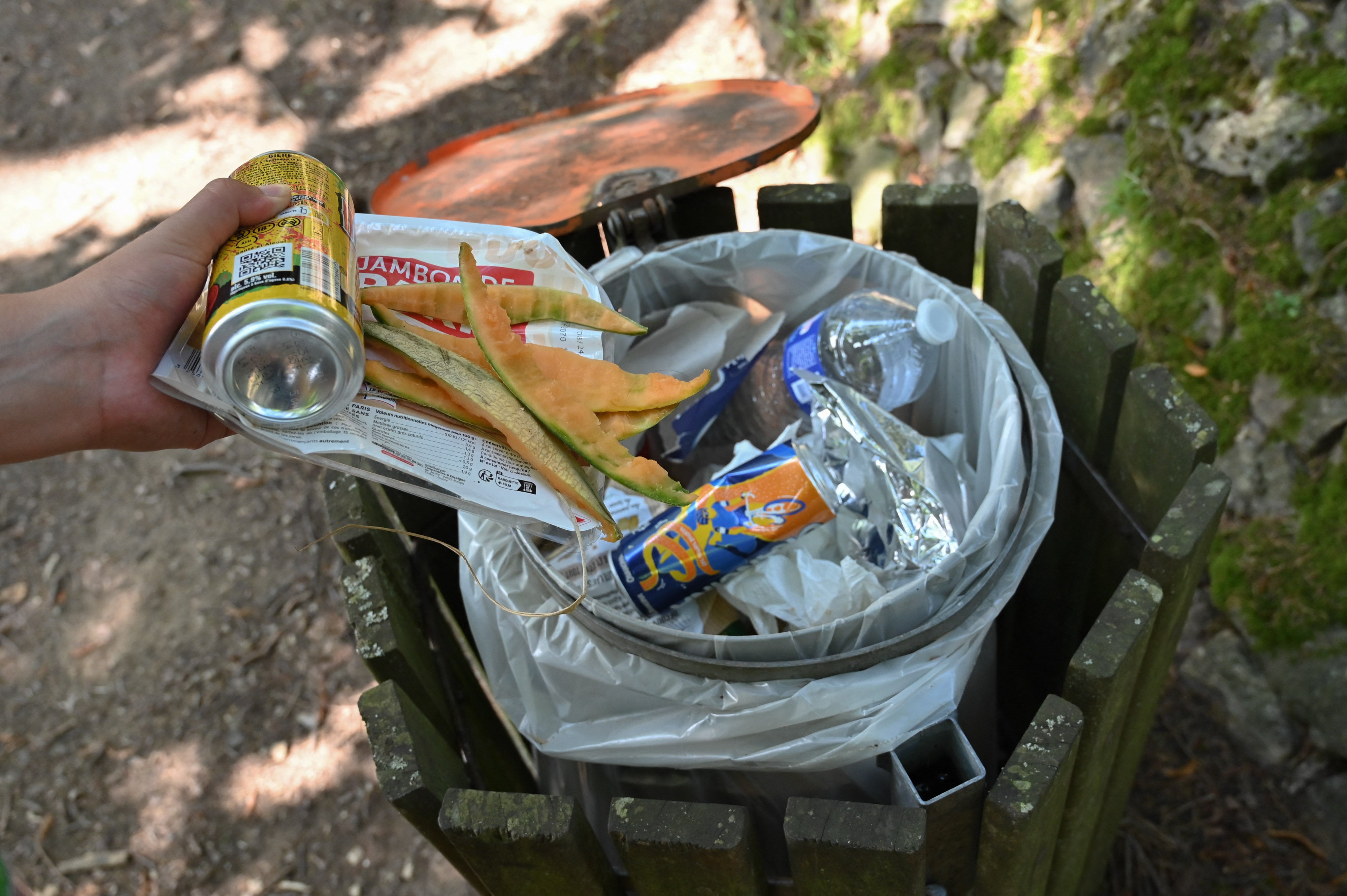 A woman throws food waste and melon skins into a public garbage can after a picnic on the shores of Ternay Lake, in Saint Marcel les Annonay, France