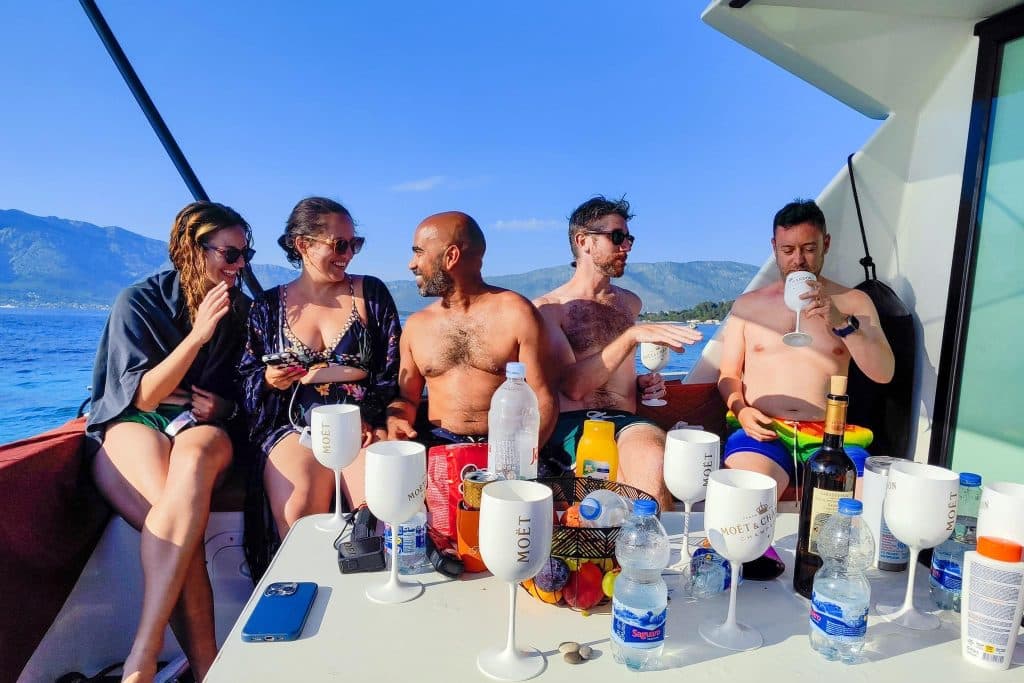 Kate and four friends sitting on the outside deck of a boat, pouring and drinking wine.