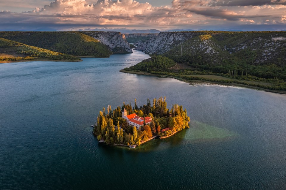 Visovac, Croatia - Aerial view of Visovac Christian monastery in Krka National Park on a bright autumn morning with dramatic golden sunrise and clear turquoise blue water