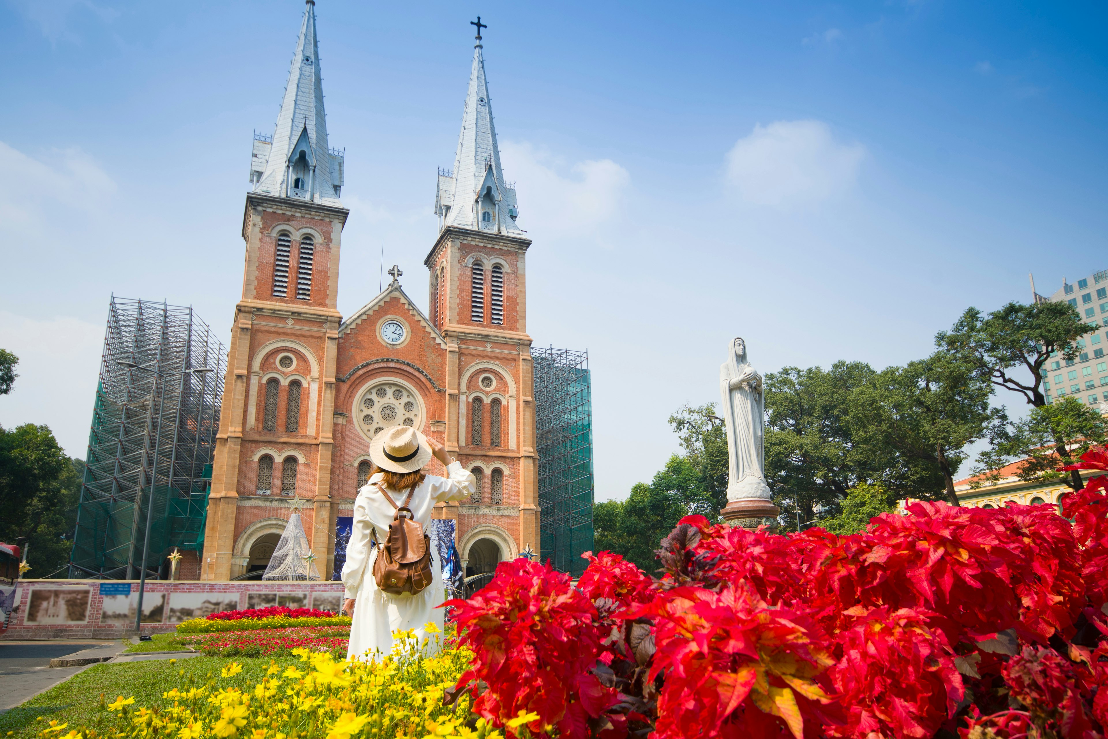 A woman stands facing a huge red-brick cathedral building with two twin towers