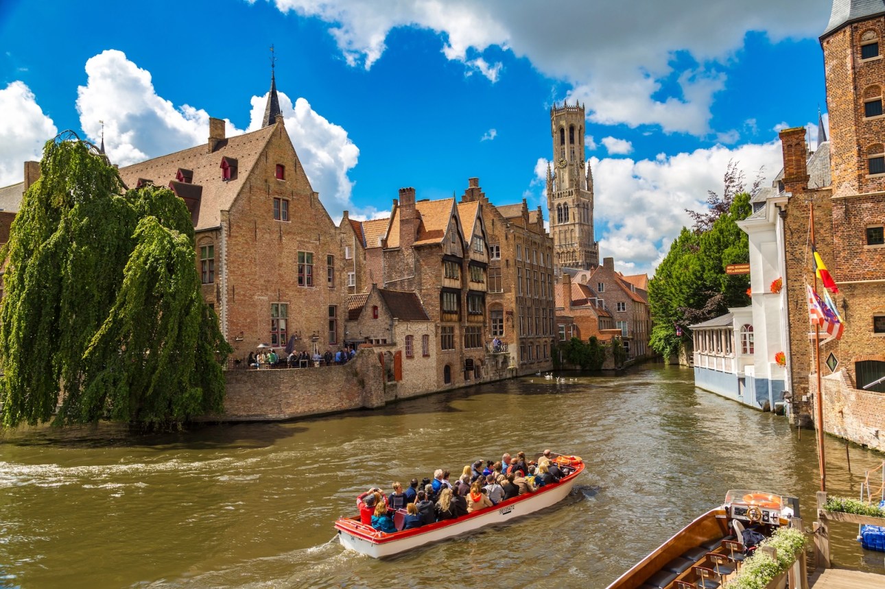 Canal in Bruges and famous Belfry tower on the background in a beautiful summer day, Belgium on June 14, 2016