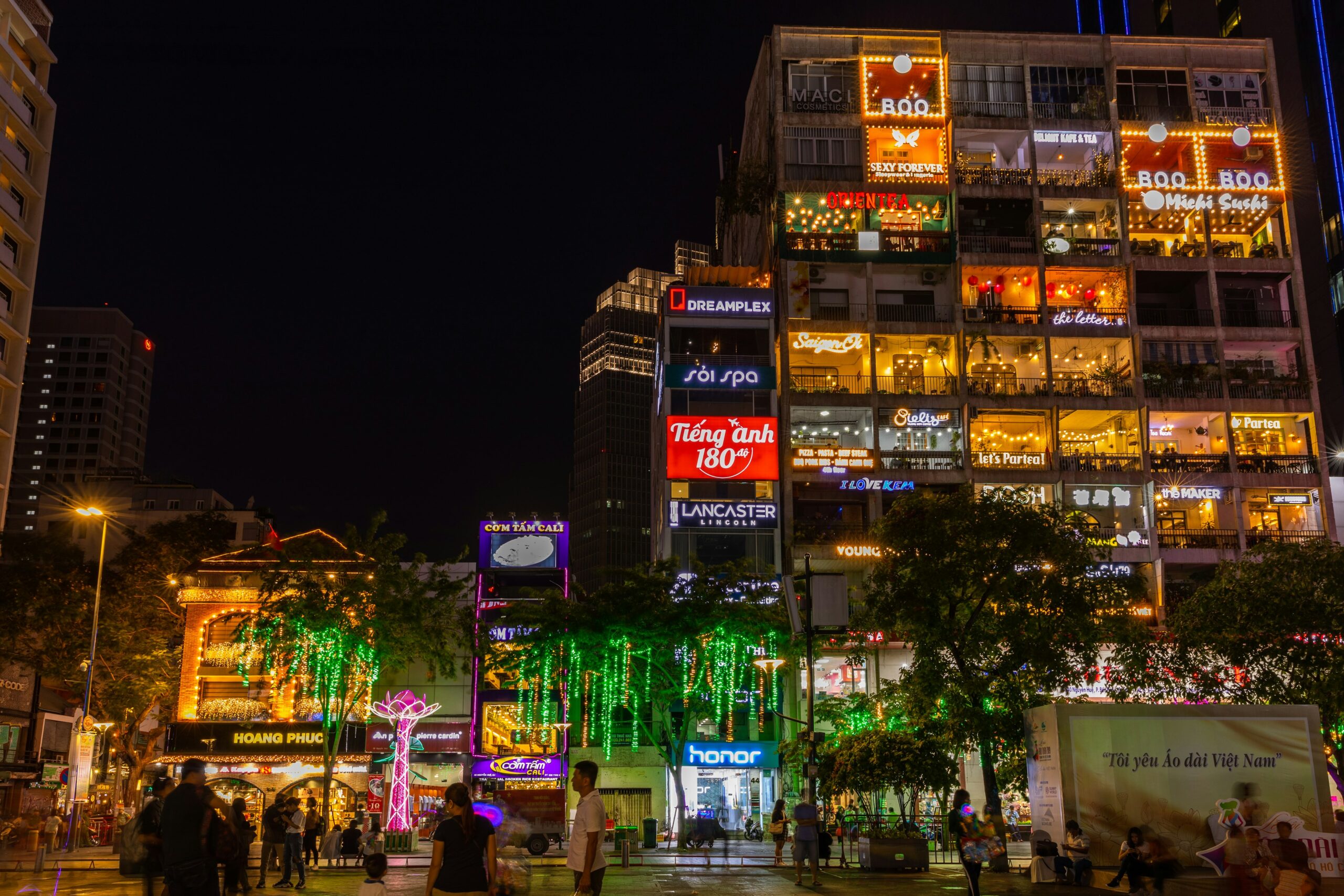 A large building exterior at night. Each balcony is lit up in neon