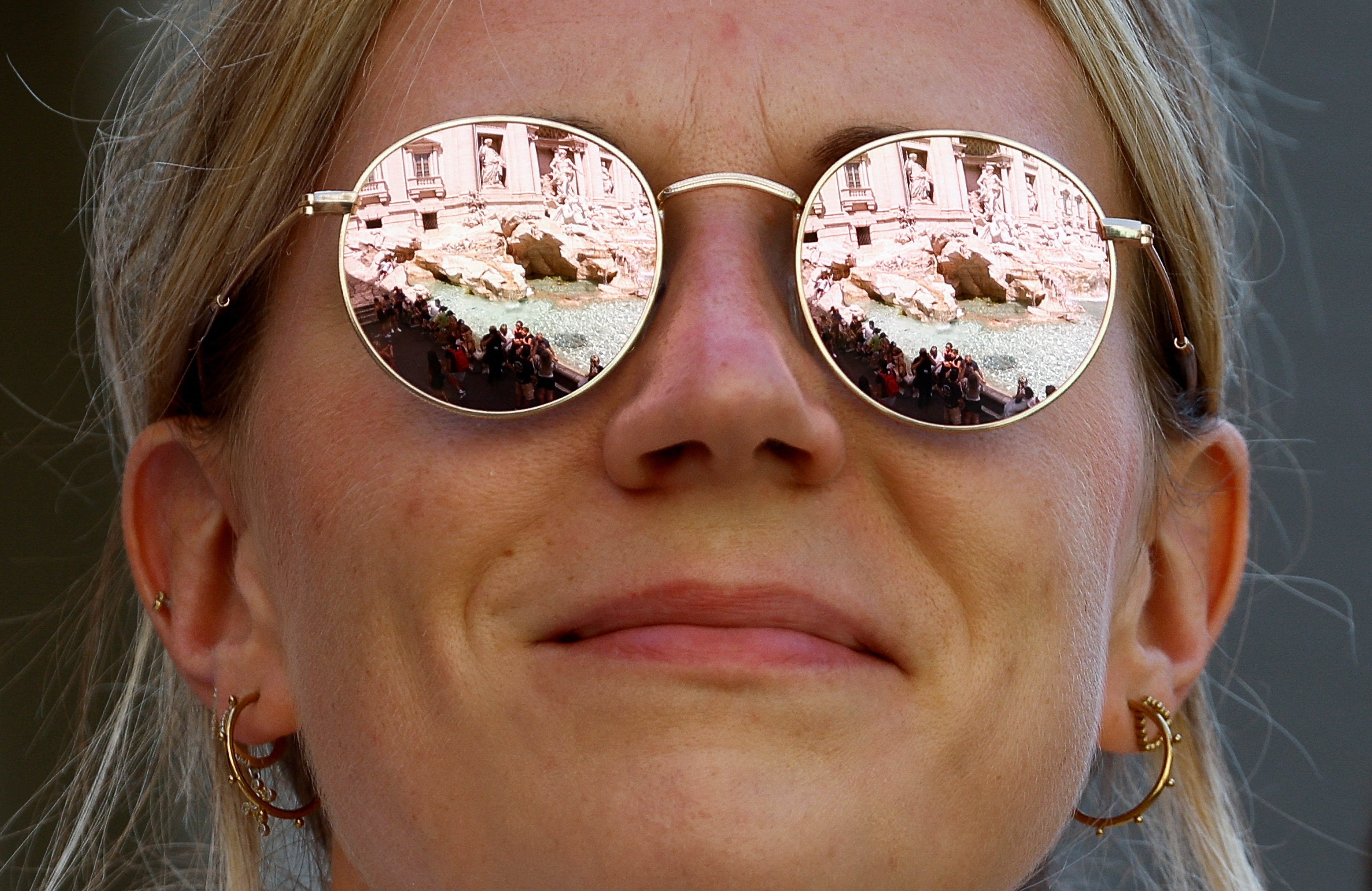 Trevi Fountain is reflected from the sunglasses of a woman during a heatwave across Italy