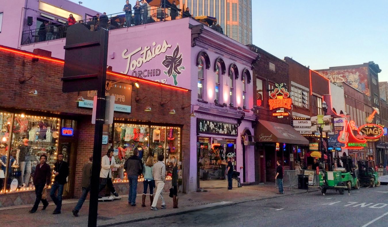 The lavender colored building of Tootsie's Orchid Lounge in the foreground on historic Broadway in downtown Nashville, lit up at night