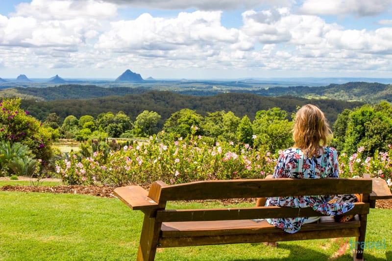 woman sitting on a bench looking at glasshouse mountains