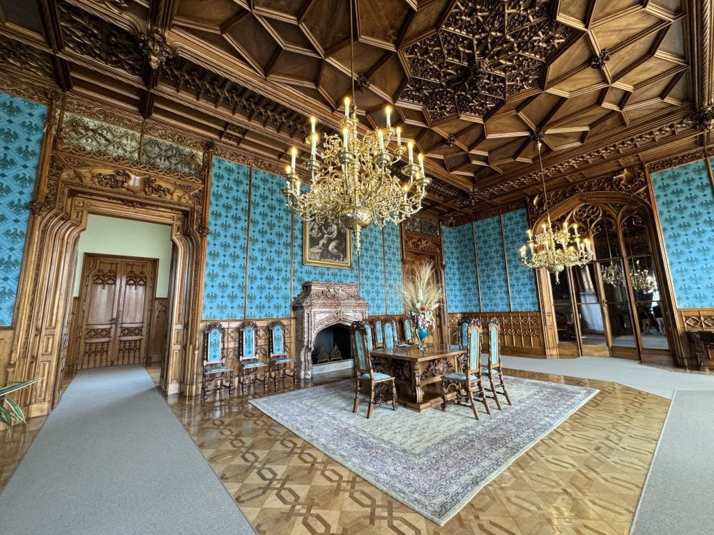 A castle with an ornate dark wood ceiling, bright turquoise walls, and hanging chandeliers.