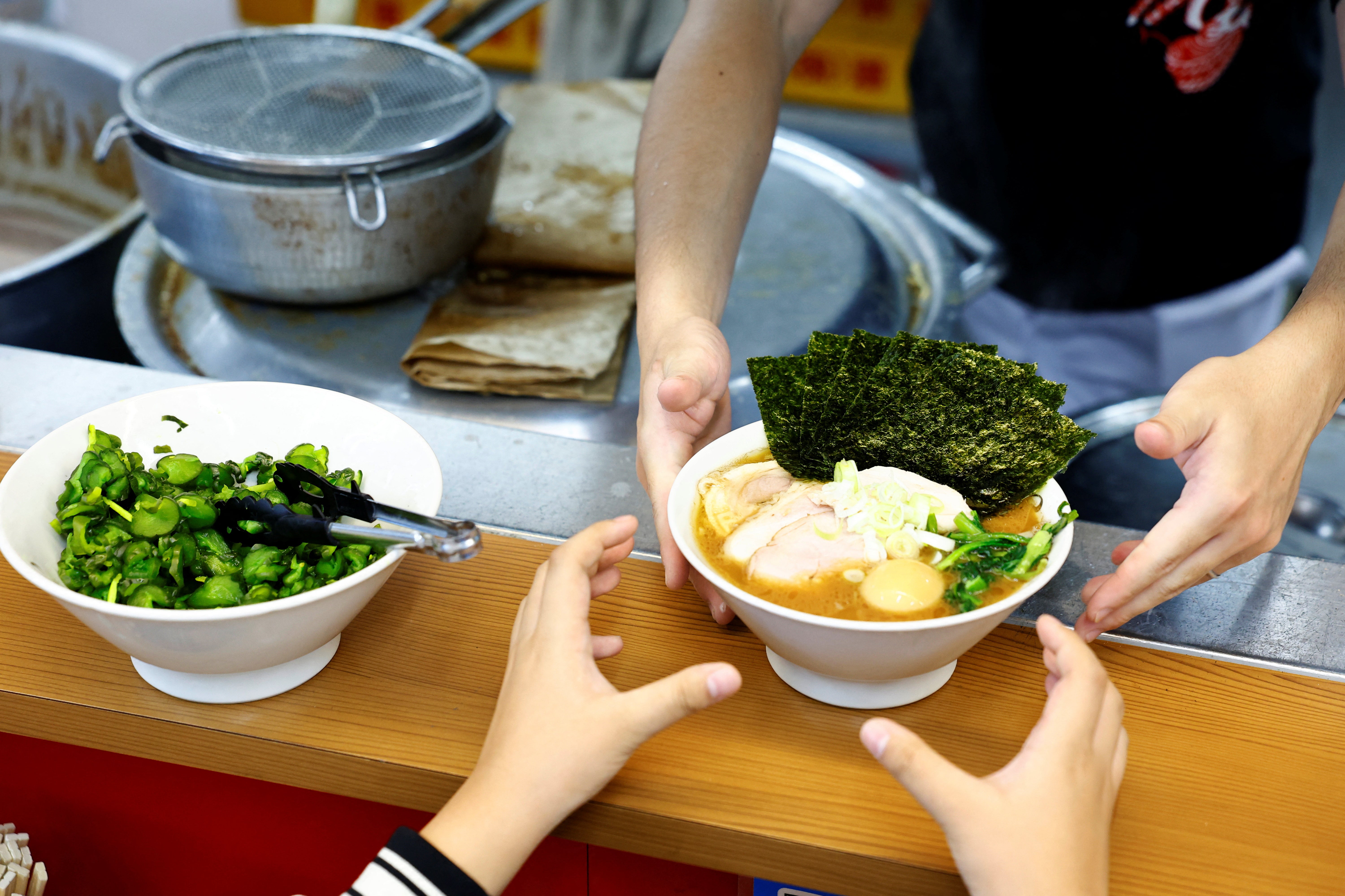 A customer receives a ramen bowl at Menya Taisei, a ramen shop, in Tokyo, Japan, October 22, 2024