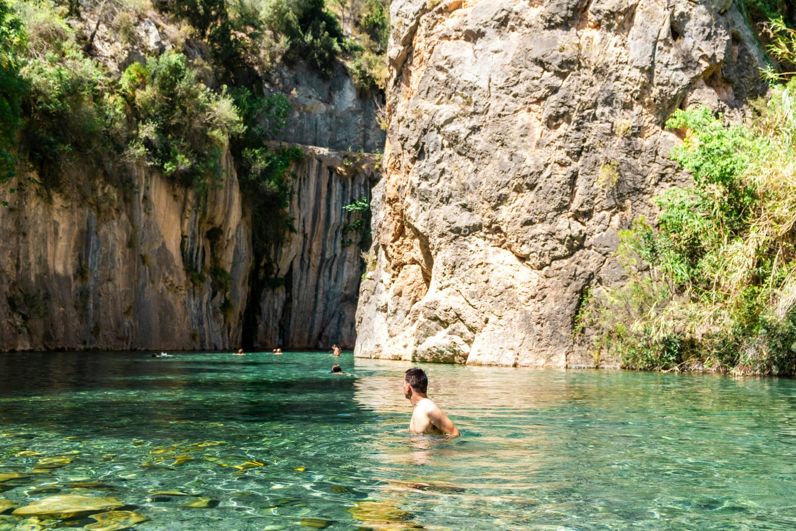 People swim in clear water in a ravine with sheer rock faces rising either side