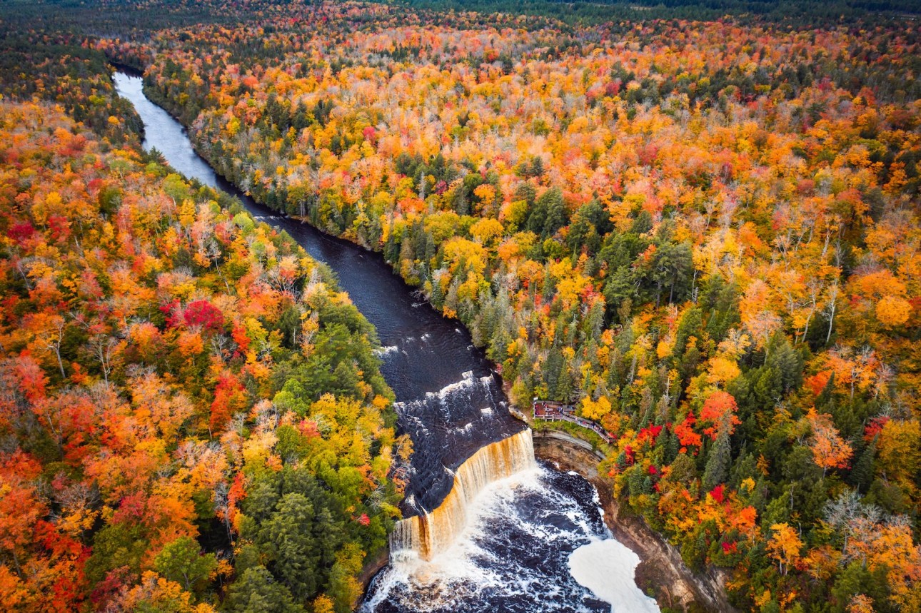 Incredible aerial photograph of the upper waterfall cascade at Tahquamenon Falls with beautiful autumn foliage on the trees with green, yellow, red and orange leaves surrounding the river.