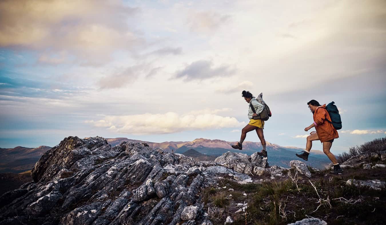 Two people with backpacks hiking across a rugged mountain trail