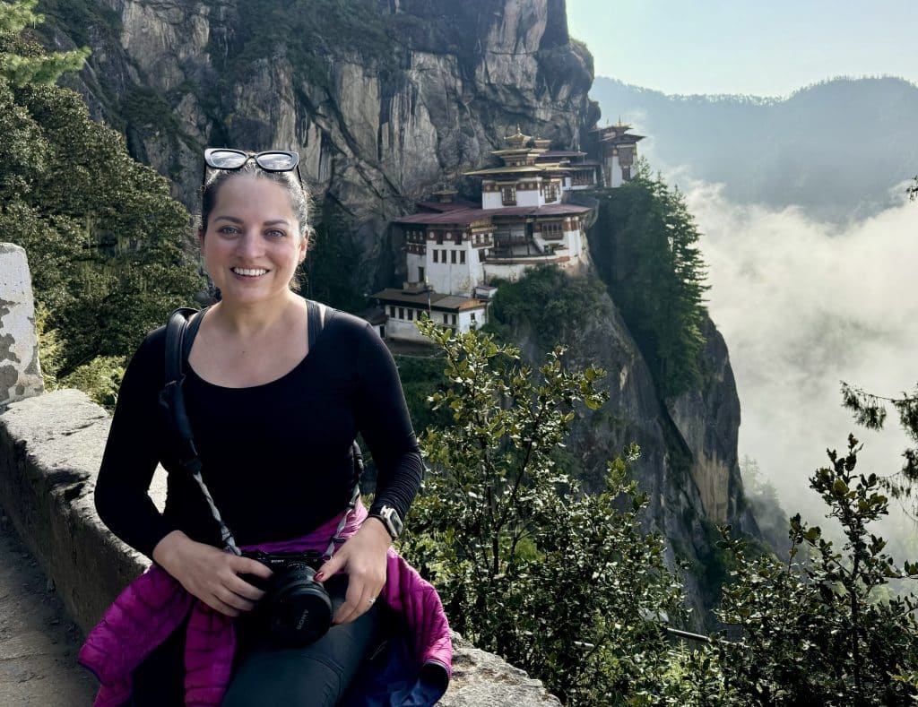 Kate posing in front of a tiny Bhutanese monastery tucked into the side of a cliff.