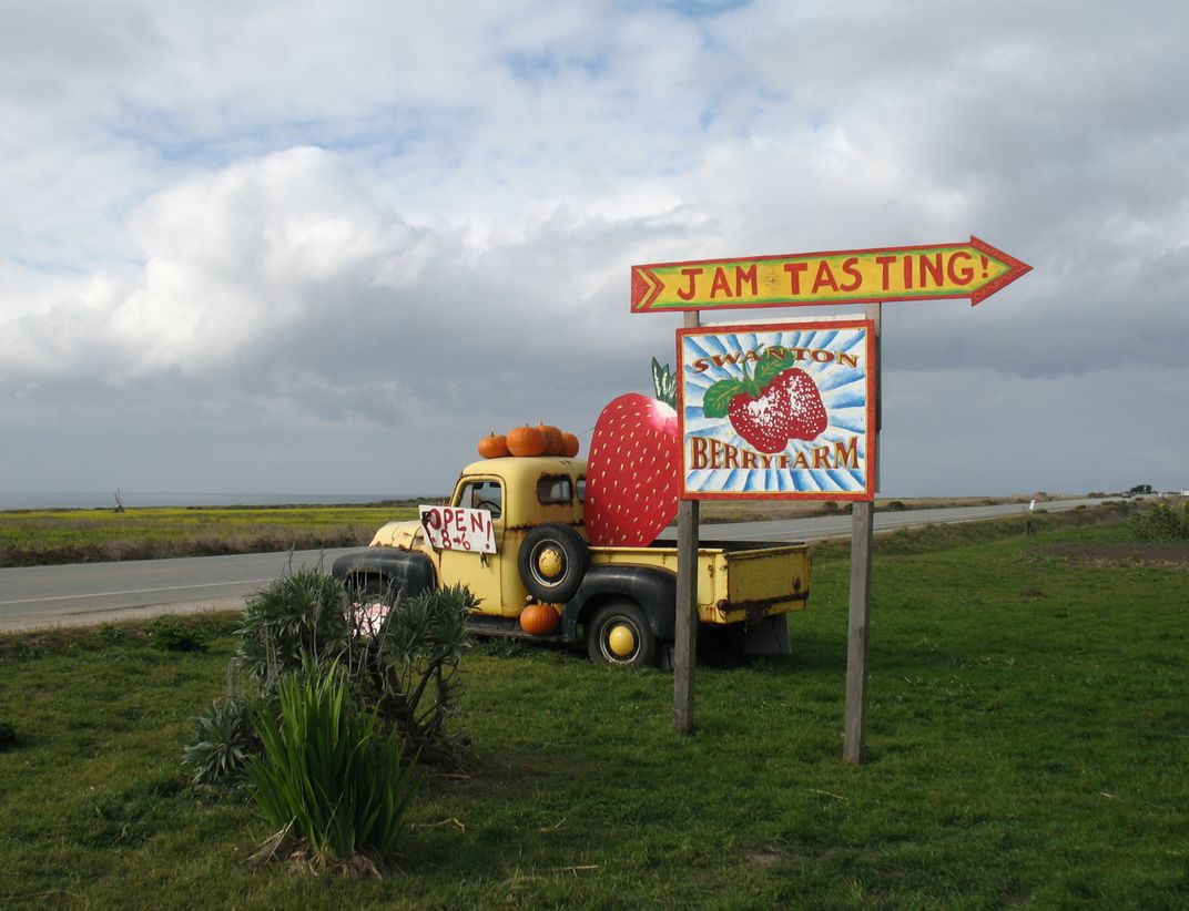 A yellow truck parked in the grass next to a Jam tasting sign