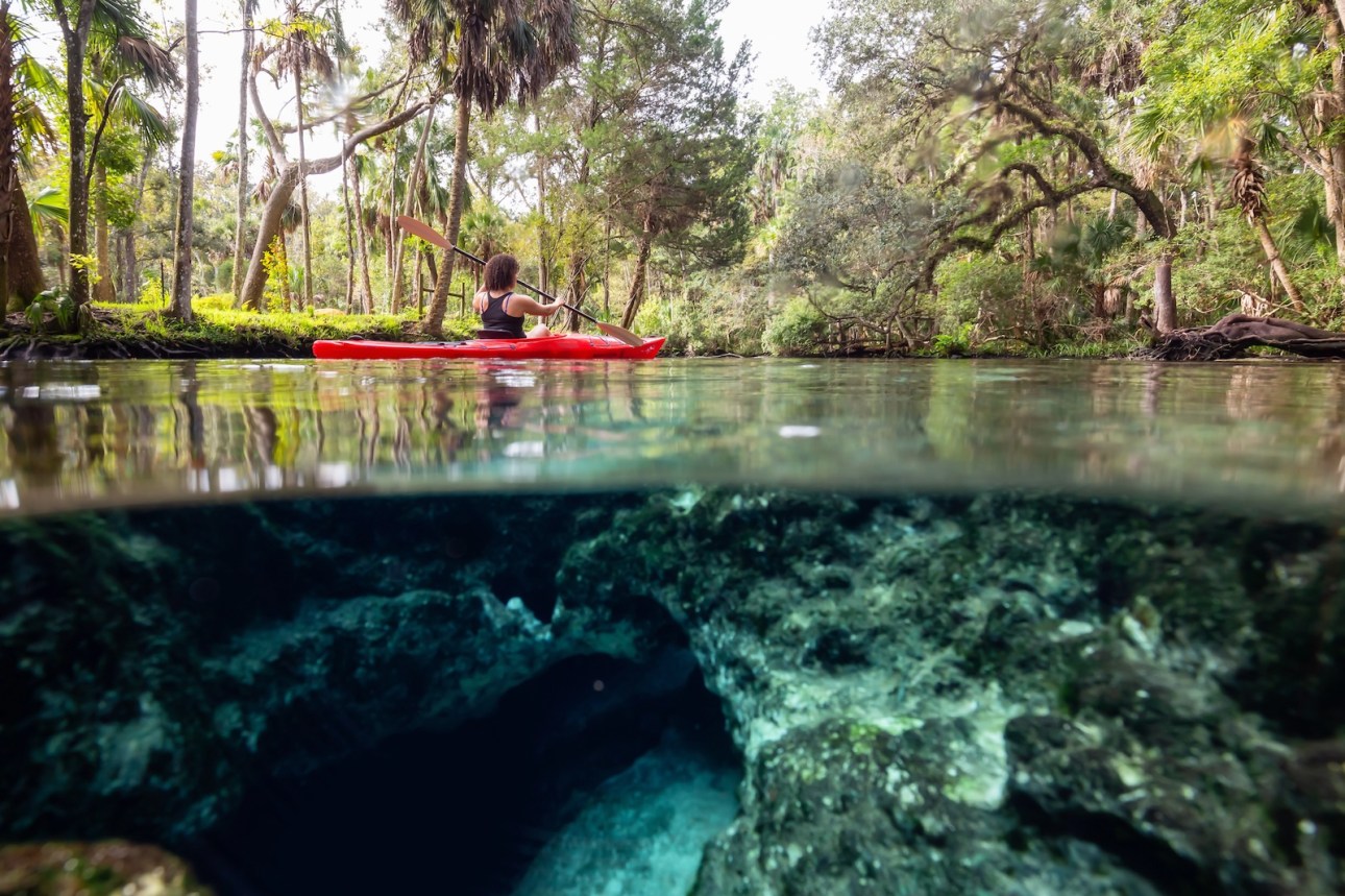 Over and Under picture of a girl kayaking in a lake near an underwater cave formation. Taken in 7 Sisters Springs, Chassahowitzka River, Florida, United States of America.