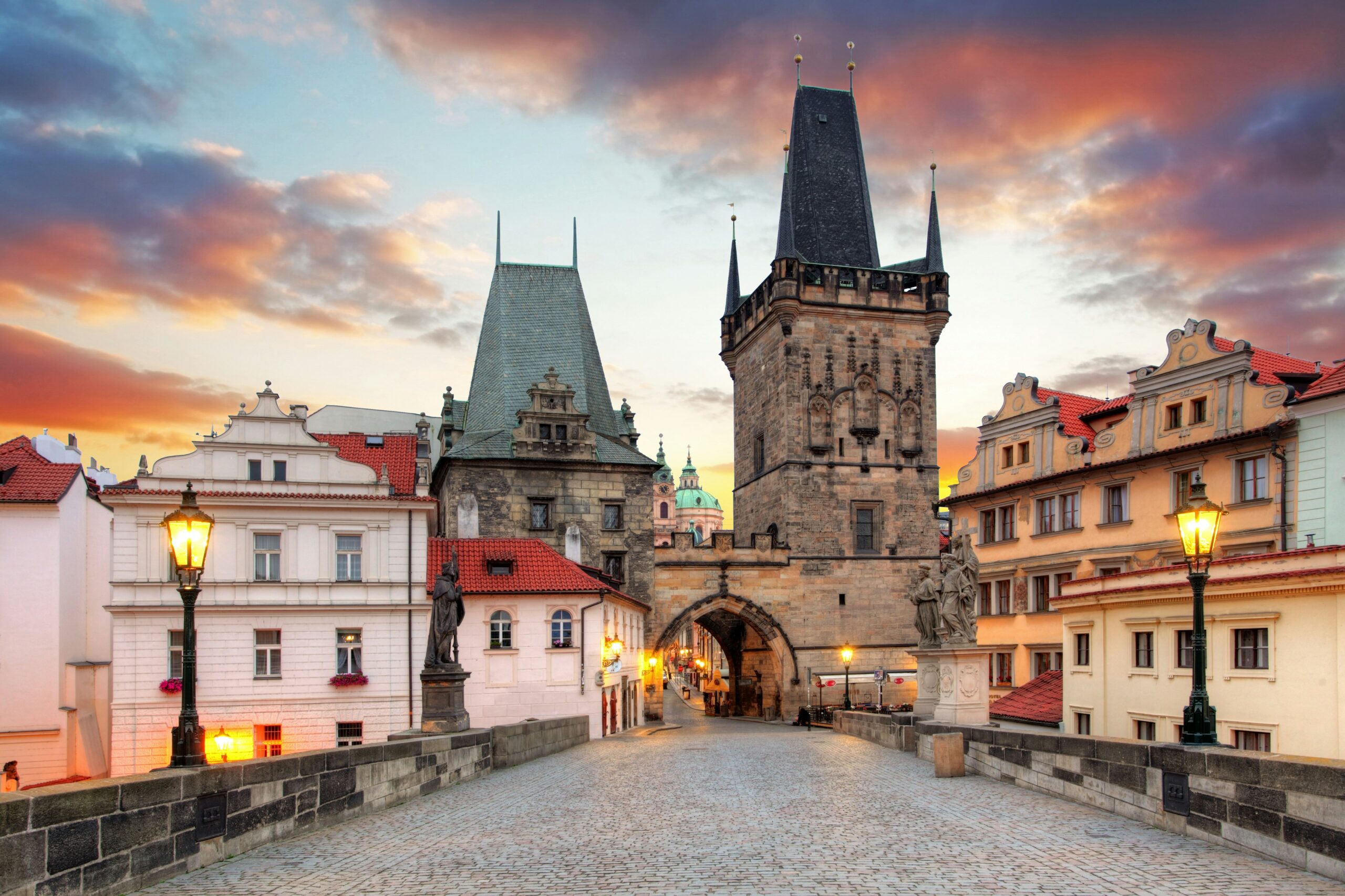 A historic cobblestone bridge leads to a medieval gate with pointed towers during sunrise