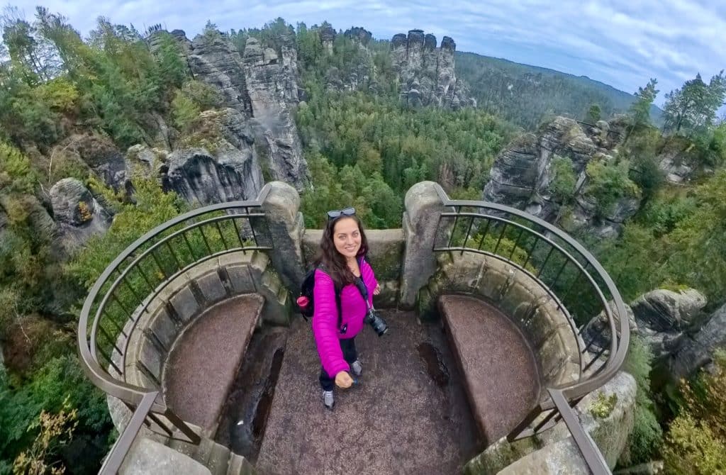 Kate standing on a stone platform overlooking a landscape of tall jagged rocks interspersed with a forest.