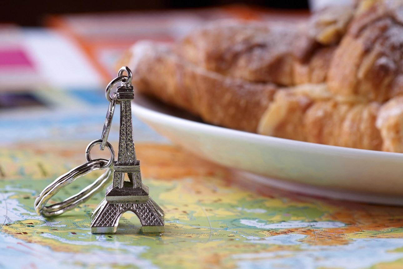 Eiffel tower keychain and croissant on maps background