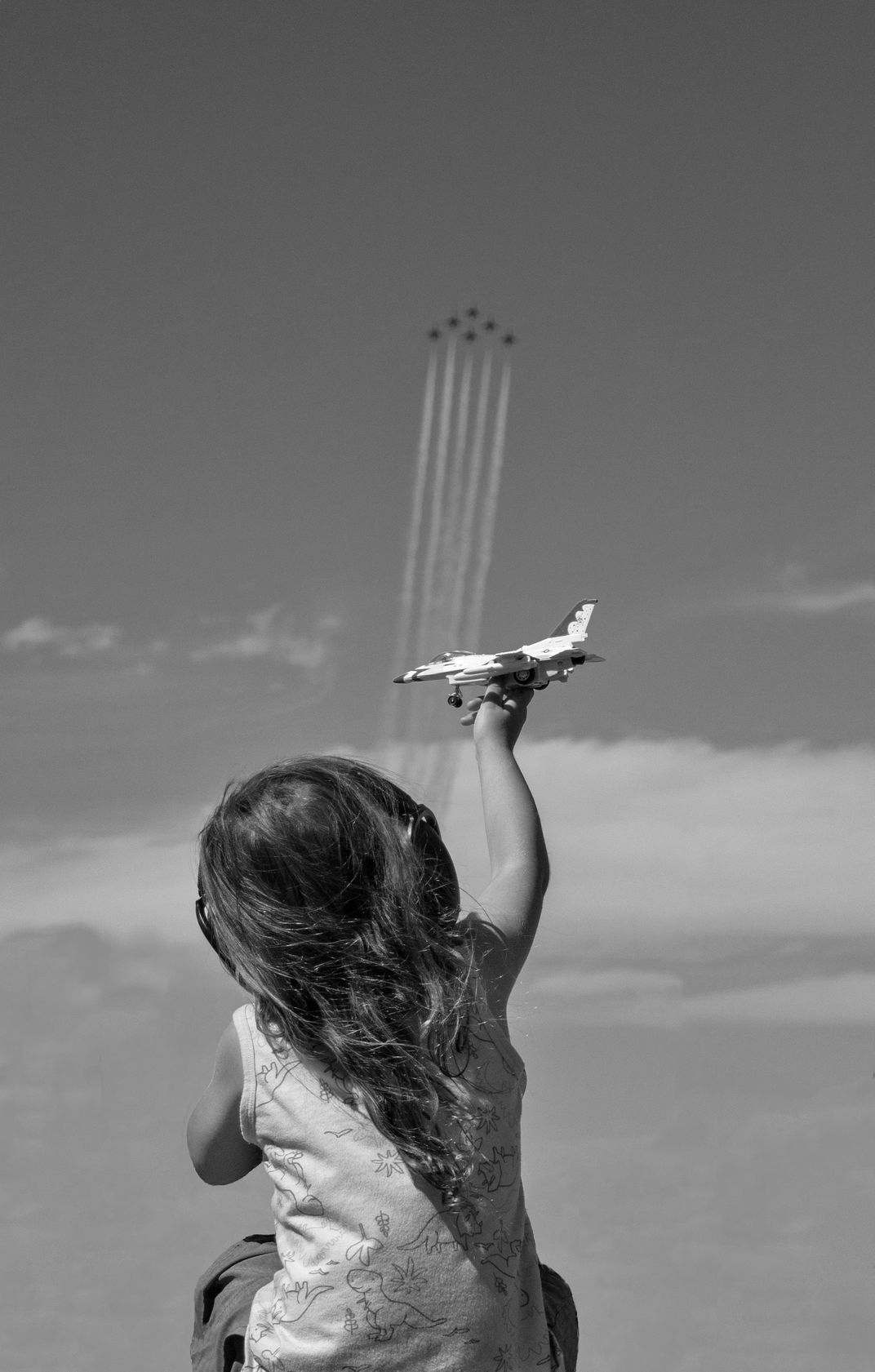 7 - A child reaches a toy plane toward the sky as pilots perform overhead at an Olympia air show.