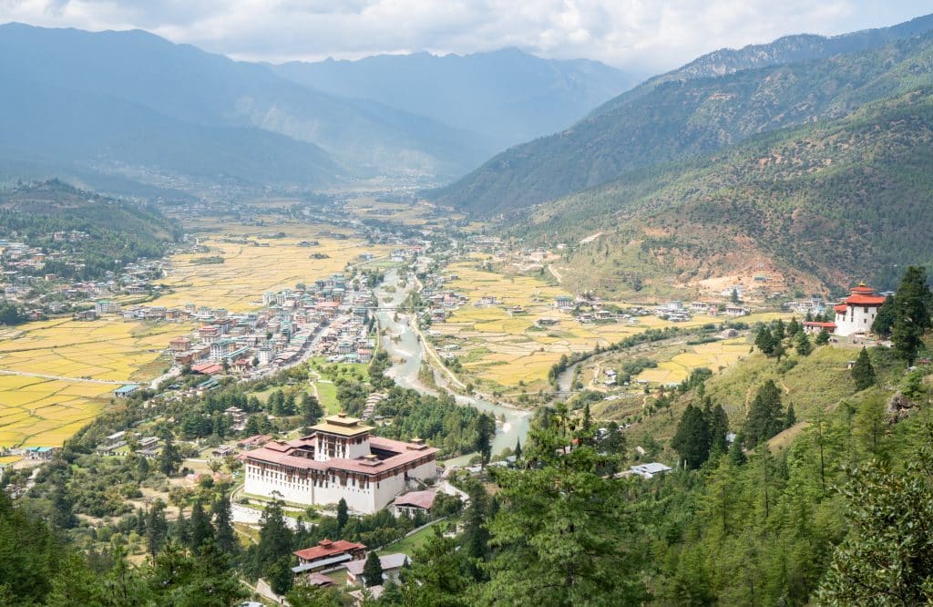 A view over a valley in Bhutan surrounded by mountains and rice paddies, a temple in the distance.