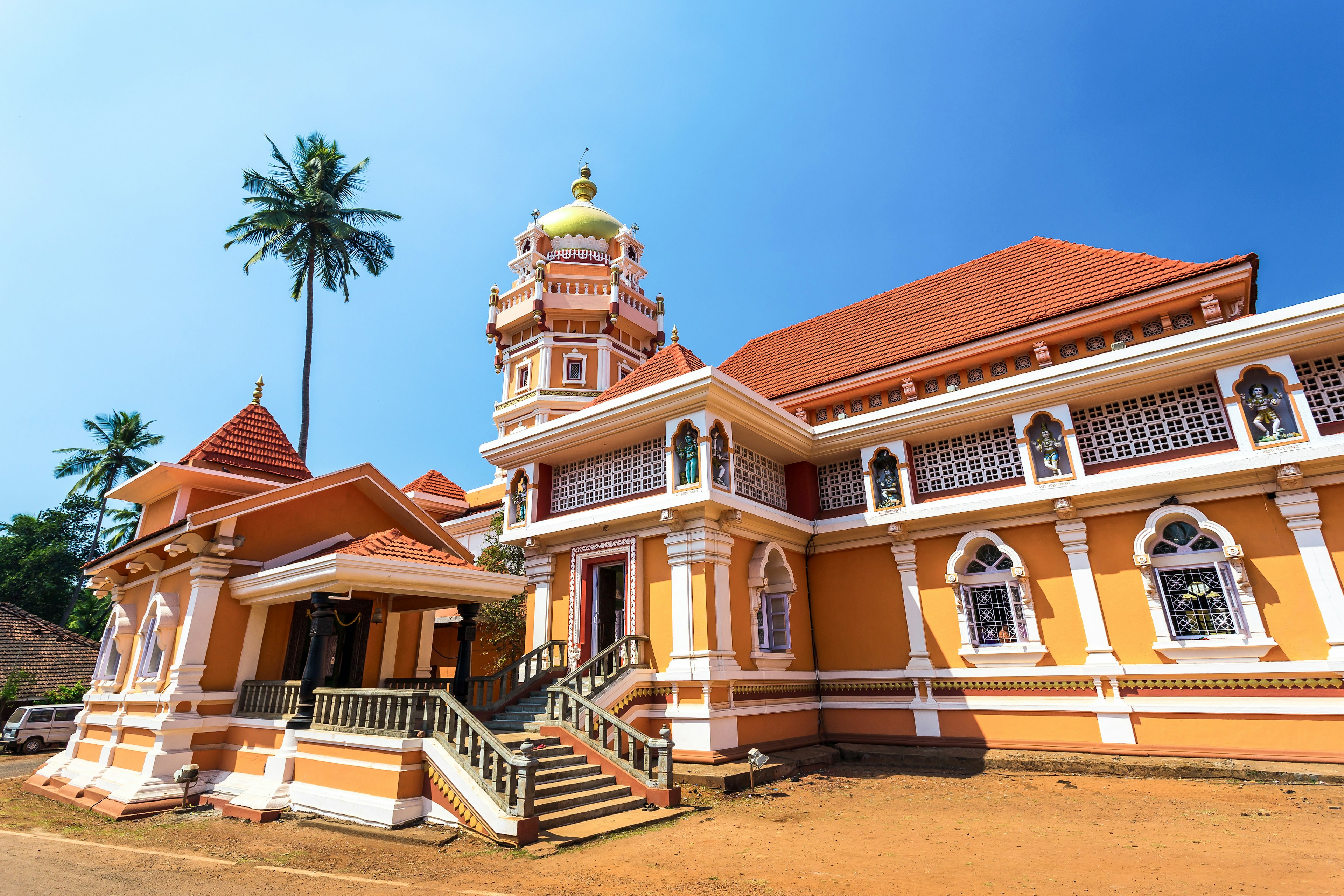 Shree Shantadurga Temple in Goa, India, painted in vibrant yellow-orange against a clear blue sky.