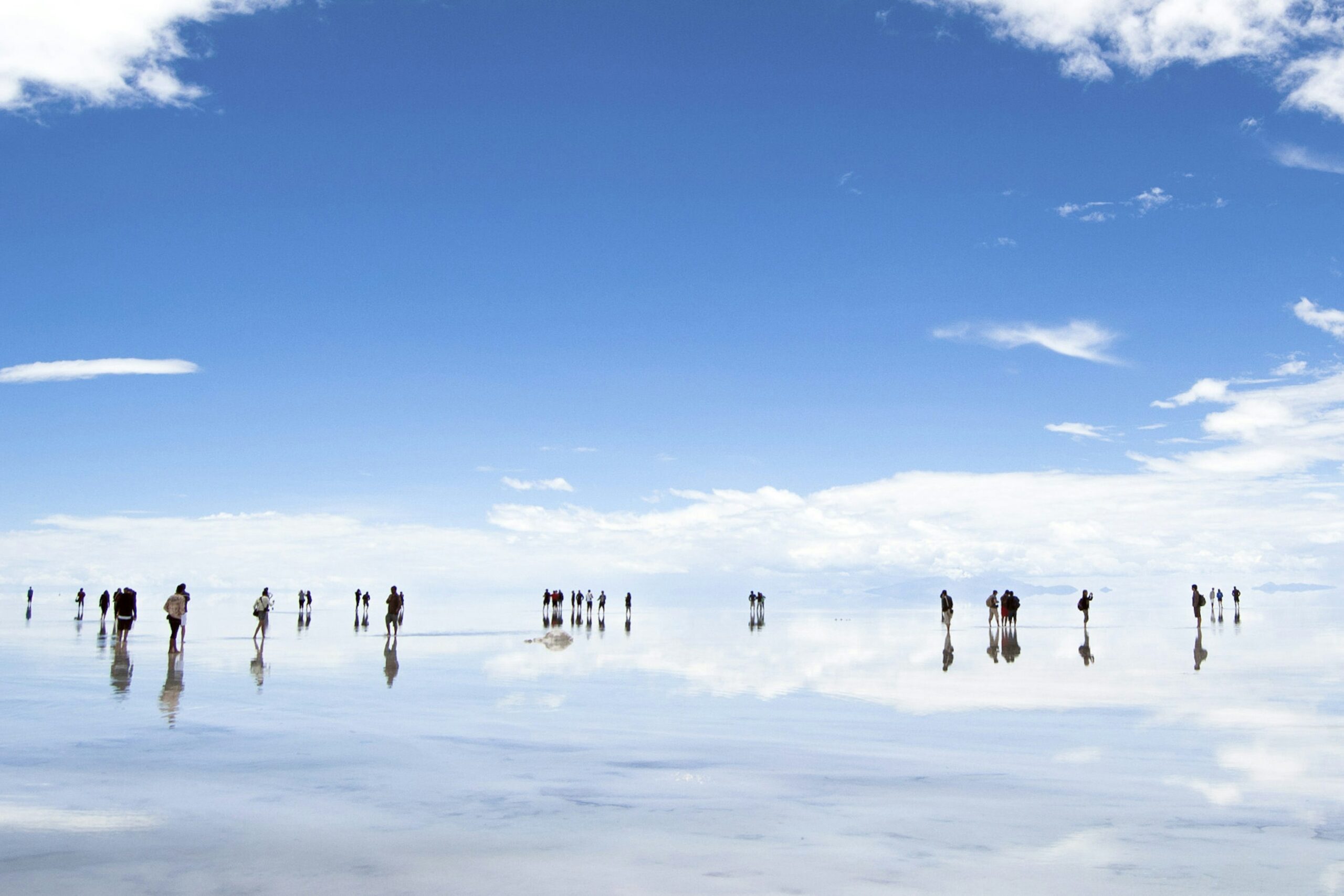 Visitors stand in shallow water of vast the salt flats where the sky and clouds are reflected in the water